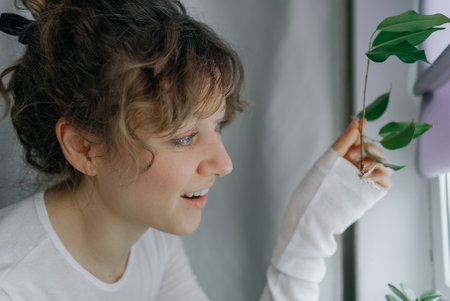 Young woman observing a plant by the windowの写真素材