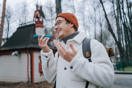 Tourist using voice assistant on smartphone while exploring city parkの写真素材