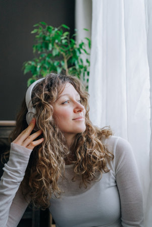 Woman listening music with headphones and looking out windowの写真素材