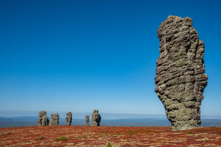 Manpupuner rock formations dominating red tundra landscape under blue sky in komi republic, russiaの写真素材