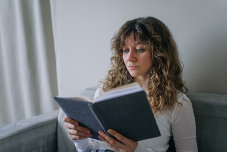 Young woman reading a book at home on the sofaの写真素材