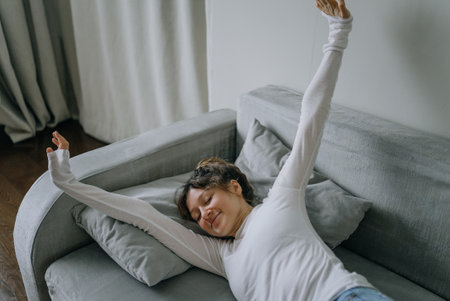 Young woman stretching on sofa enjoying peaceful morning at homeの写真素材