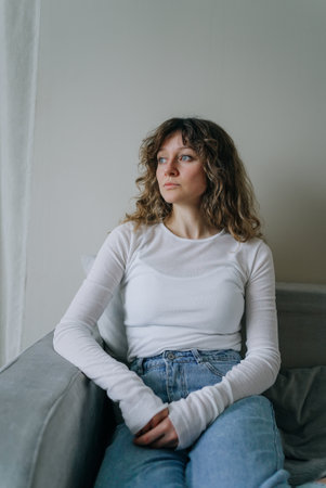 Young woman sitting on sofa contemplating near windowの写真素材