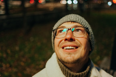 Smiling man wearing glasses and beanie looking up at night