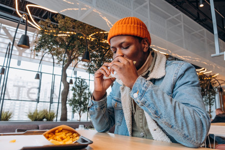 Young man enjoying a burger and fries at a modern food courtの写真素材