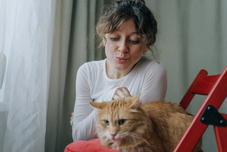 Woman making funny faces and petting ginger cat at homeの写真素材