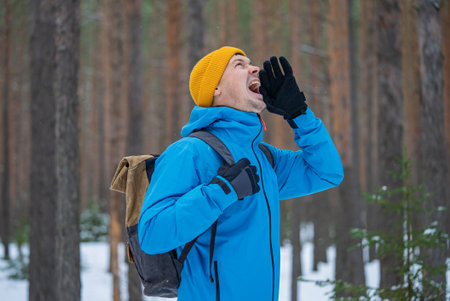 Hiker shouting in snowy forest wearing backpack and winter clothesの写真素材