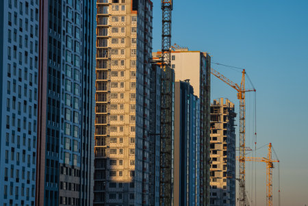 Construction cranes building modern residential buildings at sunsetの写真素材
