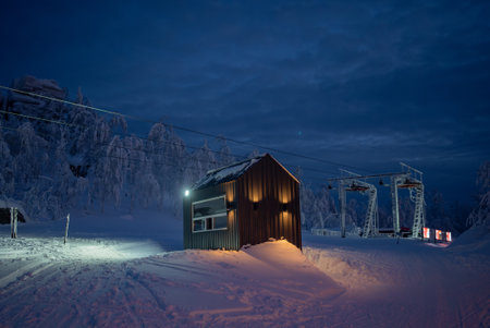 Ski lift and wooden cabin illuminating snowy mountain at duskの写真素材
