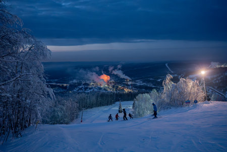 Skiers enjoying night skiing with illuminated industrial landscape in the backgroundの写真素材