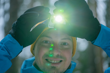 Smiling man wearing headlamp and gloves in snowy forestの写真素材