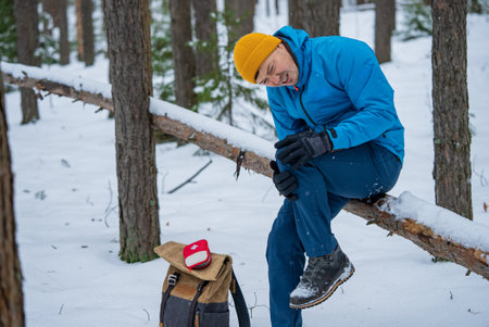 Hiker suffering knee pain in snowy forest during winter tripの写真素材