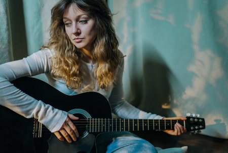 Young woman playing acoustic guitar indoorsの写真素材
