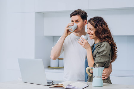 Happy couple drinking coffee and using laptop in kitchenの写真素材