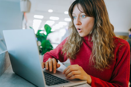 Shocked freelancer reading unexpected news on laptop in coworking spaceの写真素材