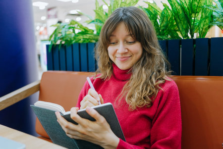 Young woman writing in notebook at cafe tableの写真素材
