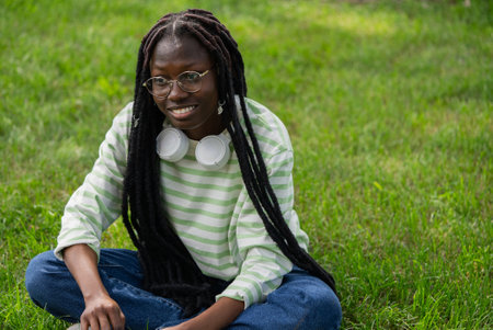 Young black woman relaxing sitting on grass wearing headphones and smiling