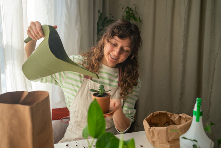Woman repotting plants at home using watering can and potting soilの写真素材