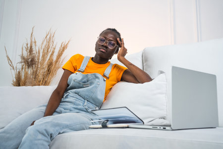 African American woman suffers from headaches while working on a laptop on the couchの写真素材