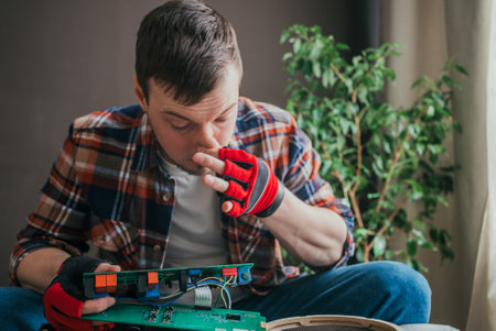 Technician wearing gloves is sitting and carefully inspecting a circuit board, smelling a strange odor that could indicate a malfunction or overheatingの写真素材