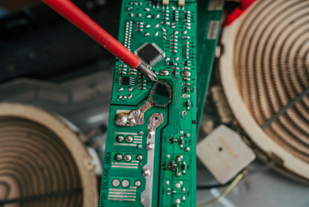 Technician uses a screwdriver to inspect a burnt and damaged electronic circuit board from a kitchen appliance, highlighting the intricate components and potential electrical hazardsの写真素材