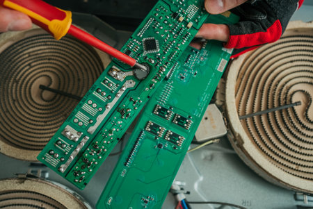 Technician fixing stove circuit board, carefully manipulating screwdriver while diagnosing electrical system malfunctionの写真素材