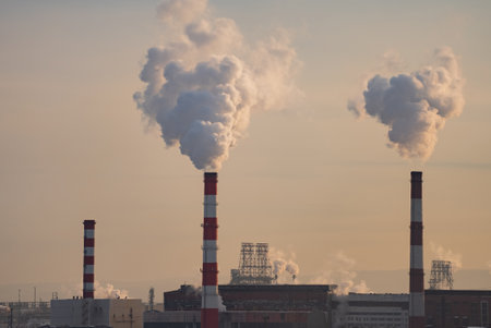 Billowing smoke from industrial smokestacks rising against dramatic sunset colors, symbolizing environmental challenges and industrial pollutions visual intensityの写真素材