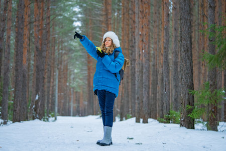 Hiker using smartphone and pointing finger in snowy forest trailの写真素材