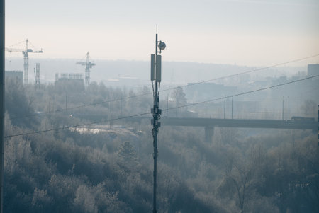 Communication tower standing near industrial site, foggy environment surrounding construction cranes and highway bridge, representing technological infrastructure growthの写真素材