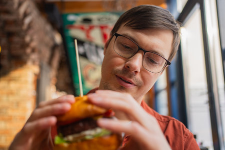 Customer enjoying a delicious burger in a bustling restaurant, savoring every bite during a lunch break, feeling satisfied with the quality of food and attentive serviceの写真素材