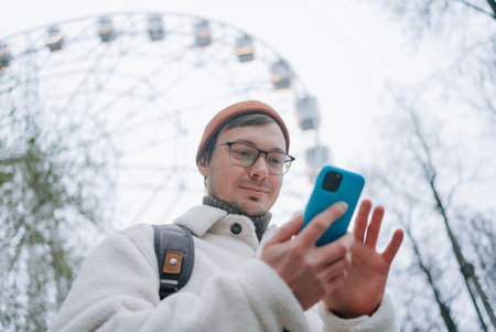 Tourist using smartphone near ferris wheel in amusement park