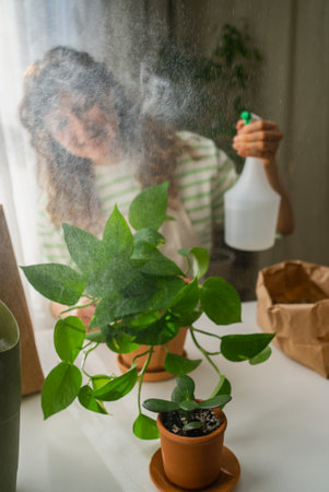 Woman spraying water on houseplants enjoying her hobby at homeの写真素材