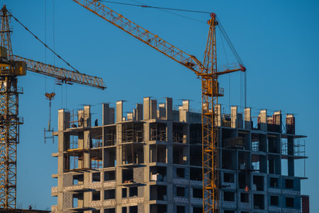 Construction cranes building modern residential apartment building under blue skyの写真素材