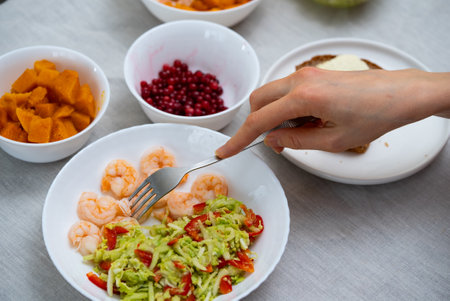 Woman eating nutritious shrimp salad with pumpkin, cranberries, and buttered bread, focusing on balanced dietary choices and fresh ingredientsの写真素材