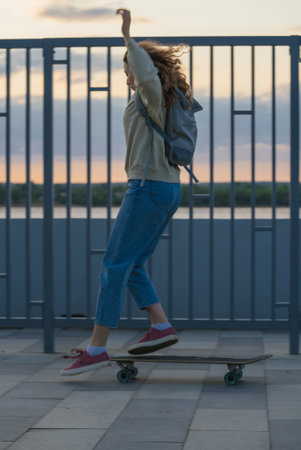 Young student skateboarding near river embankment, capturing urban energy during golden sunset light, embodying youthful freedom and adventureの写真素材