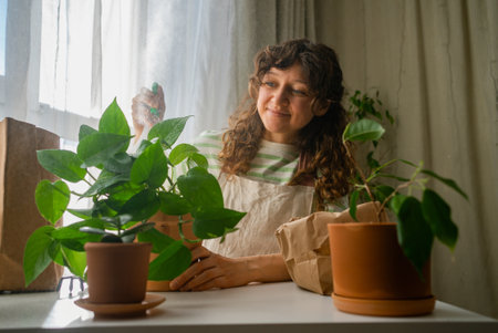 Woman spraying houseplants with water near window in bright cozy roomの写真素材