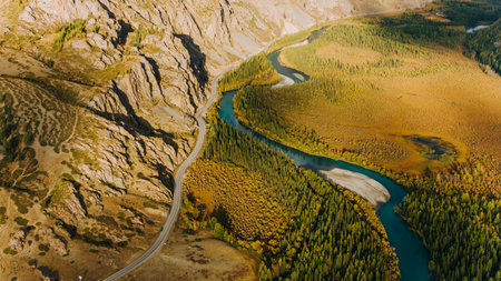 Winding river flowing through scenic mountain valley with road alongsideの写真素材