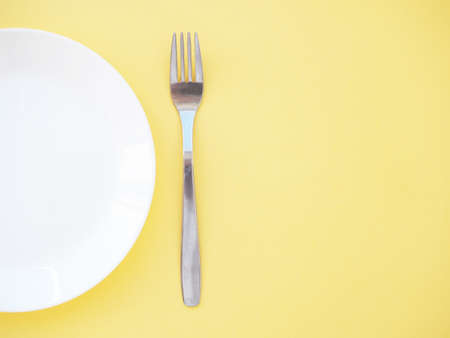 empty white plate and fork on a yellow background