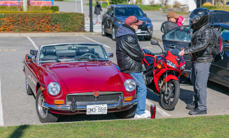 Two old man talking in front of a car in a street parking lot. One with the bike and one with the...