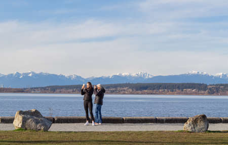 Two women tourist taking photo on sea beach with mobile smart phone camera at the park in White...