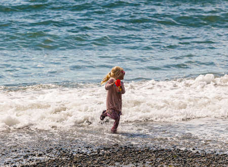 little smiling girl playing in the waves of the sea. Street view, travel photo, copy space, selective focus, concept photo happy child. Vancouver Island, BC, Canada-August 9,2021のeditorial素材