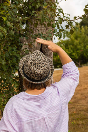 Woman in a hat looks ap on a tree in the forest, autumn season. Street view, travel photo, selective...