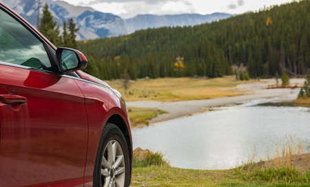 Red car parked in front of lake or river with mountains in cloudy day. Banff National Park. Travel photo, selective focus, blurred background, concept photo travelの写真素材