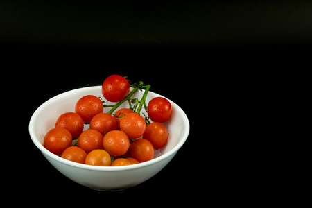 Branch of ripe cherry tomatoes on plate, top view in the black background. Fresh tomatoes in tha dark background. Selective focus, nobody, copy space for textの写真素材