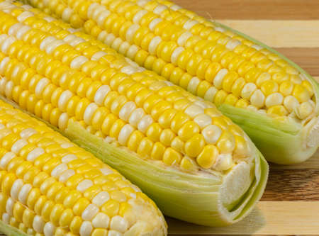 Fresh corn on cobs on wooden table, closeup. Sweet corns on wooden board. Top view, selective focus,...