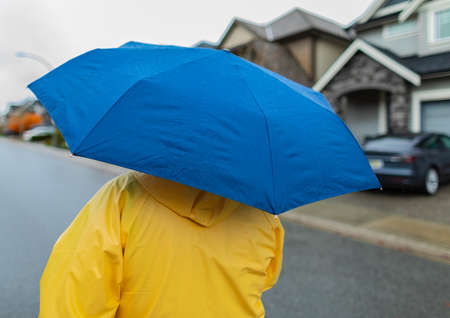 Rainy day. Woman holding blue umbrella and walking in the rain on a street. Unrecognizable person in...