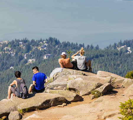 A group of young hikers sitting on a cliff and enjoying the view from the Eagle Bluffs in Cypress Provincial Park, Canada. Concept photo hiking, copy space for text, selective focus, travel photo.のeditorial素材