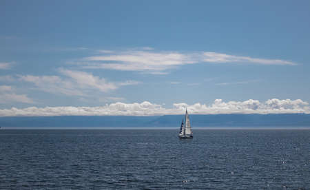 Lonely yacht with white sail in open sea. Sailboat in the Pacific Ocean near Vancouver Island, BC, Canada-July 22,2021. Selective focus, travel photo, copy space for textのeditorial素材