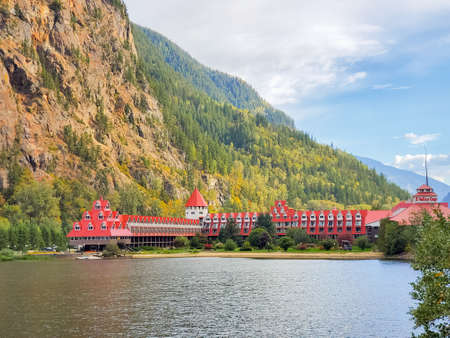 Beautiful landscape of a mountain and lake with red buildings on a shore. Three Valley Gap Lake Chateau Hotel, BC, Canada-September 26,2021. Travel photo, selective focus, nobody, mobile photoのeditorial素材