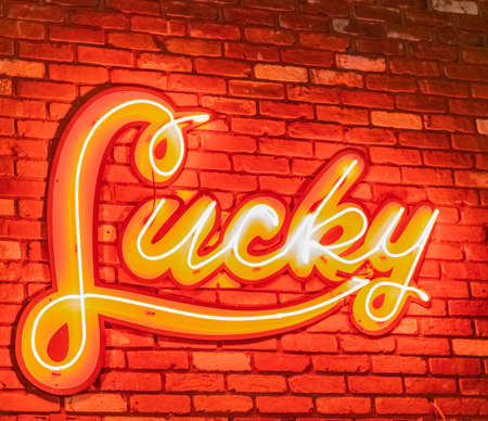 Neon sign Lucky Light banner, glowing neon signboard on brick wall. Illustration depicting neon signage with a lucky concept. Street photo, selective focus, blurredの写真素材